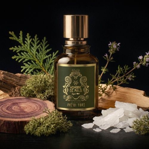 Un frasco de perfume de color verde oliva con tapón dorado y etiqueta en un marco verde oscuro.