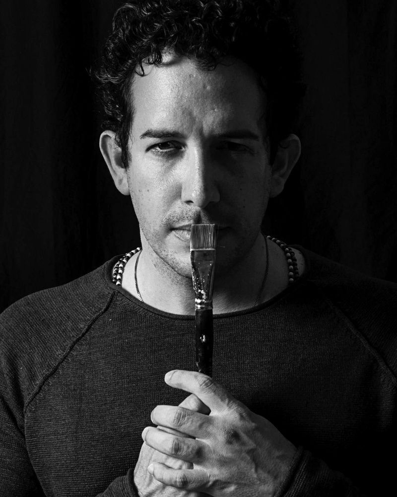 Un hombre sostiene un pincel en sus labios, retrato en blanco y negro.