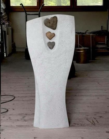 weiße Steinskulptur mit drei dunklen Herzen