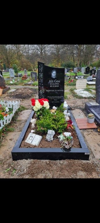 Ein Grab mit Blumen und einem Buch darauf auf einem Friedhof.