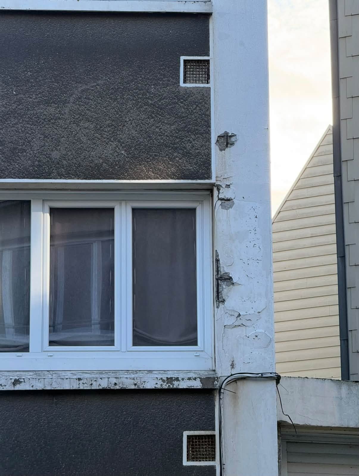 Gros plan sur l’extérieur d’une maison, avec une fenêtre et une peinture écaillée, à côté du mur d’une maison voisine