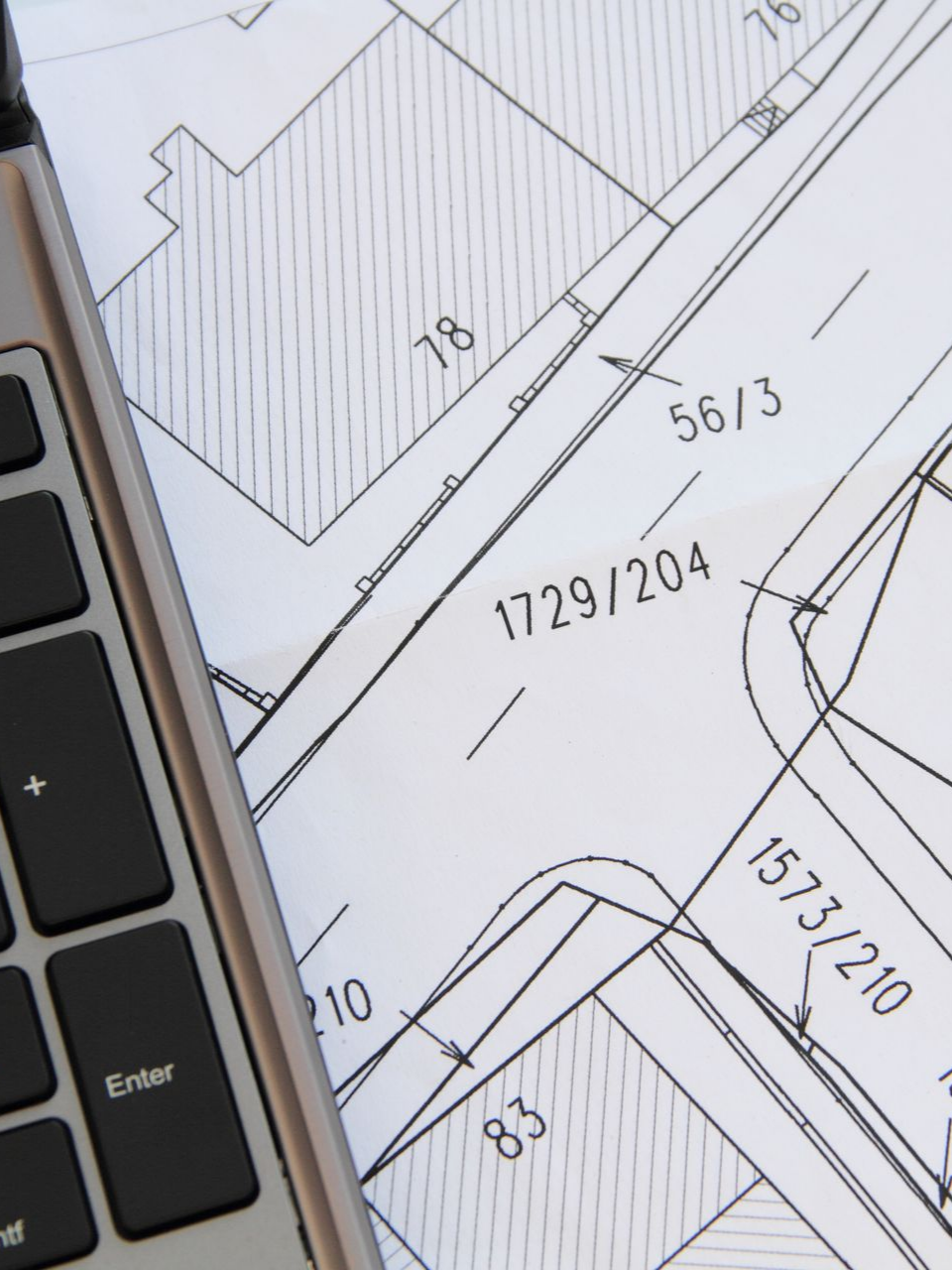 Gros plan d’un ordinateur portable à côté d’un plan immobilier indiquant les numéros des lots et les contours des bâtiments