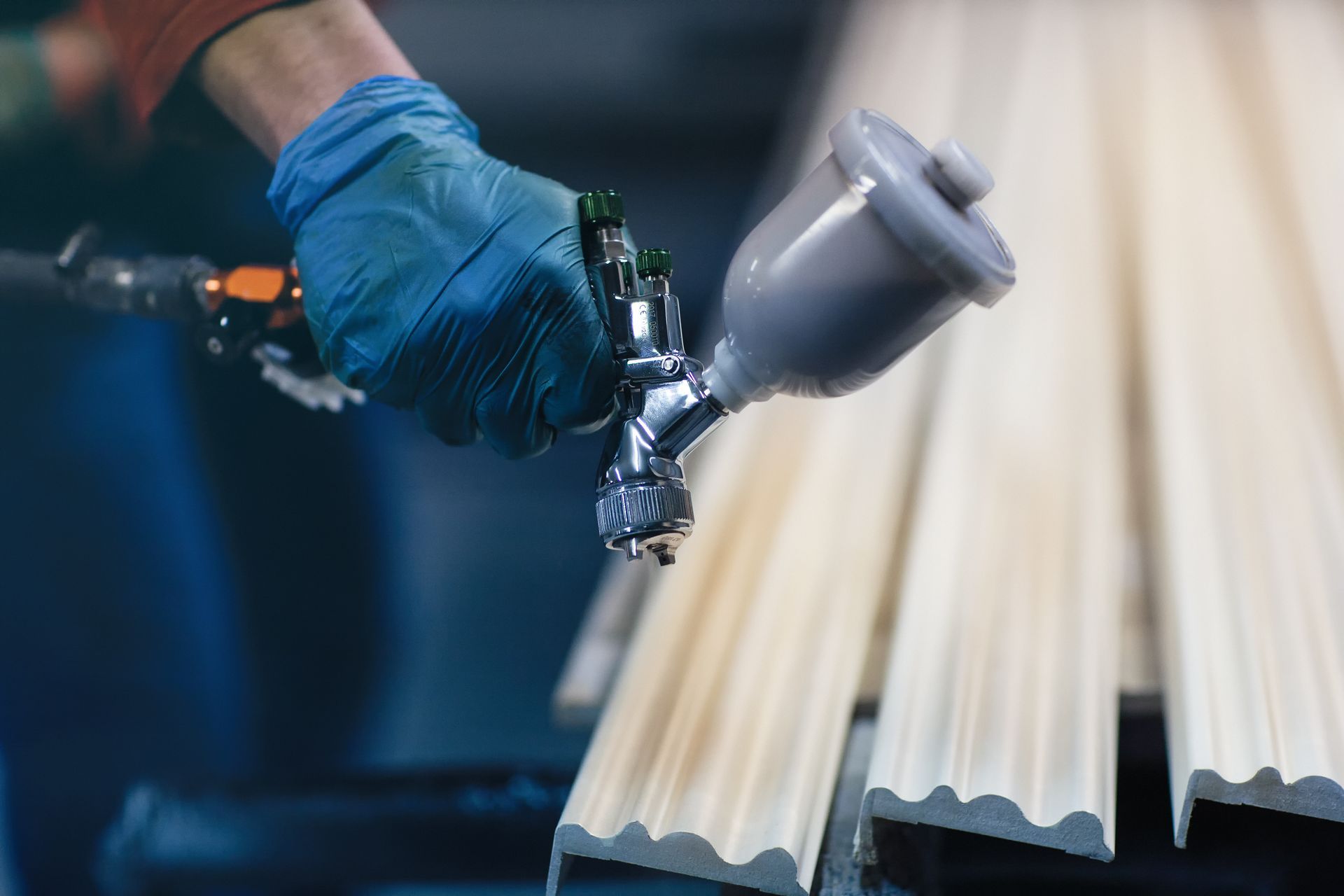 Main gantée pulvérisant de la peinture blanche sur des panneaux ondulés à l’aide d’un pistolet