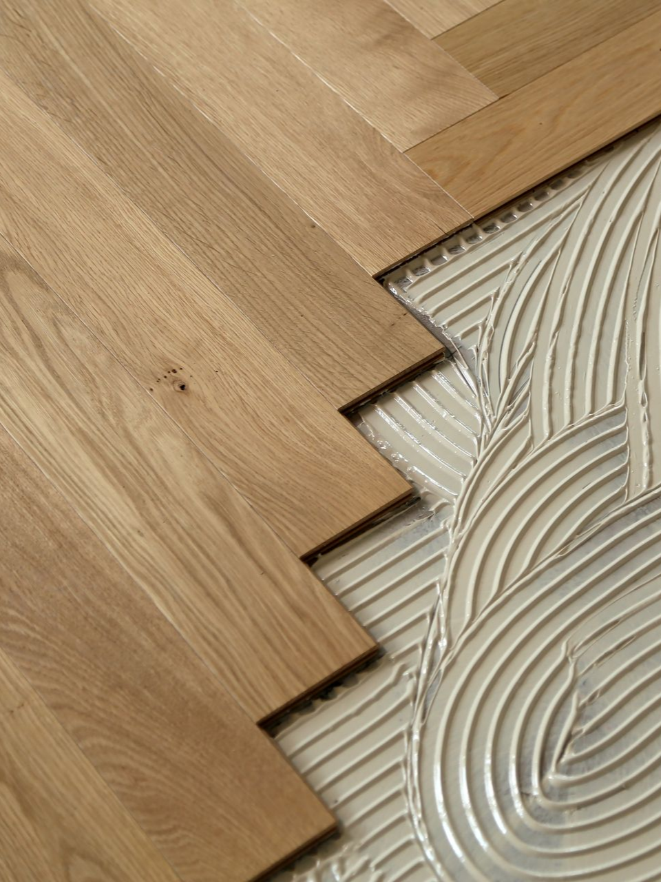 Des lames de parquet posées sur du mortier-colle blanc strié à la truelle crantée