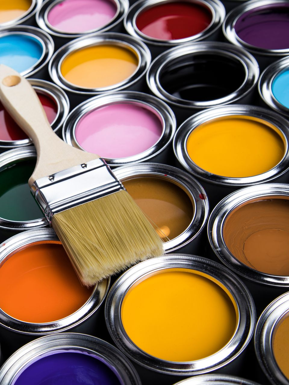 Plusieurs pots de peinture de toutes les couleurs ouverts et alignés avec un pinceau posé par dessus