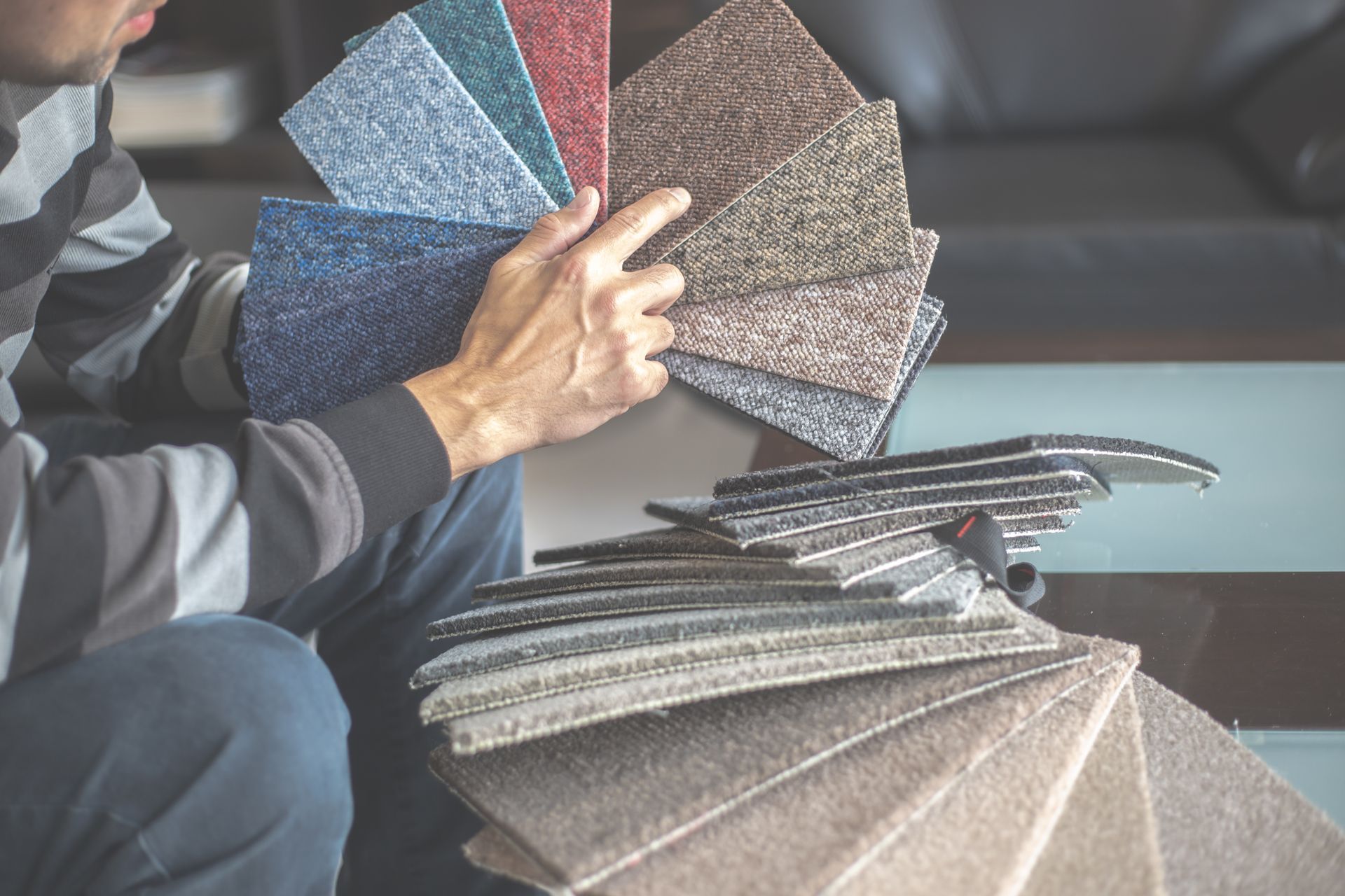 Personne feuilletant des échantillons de moquette dans une salle d’exposition, avec des textures grises et bleues visibles