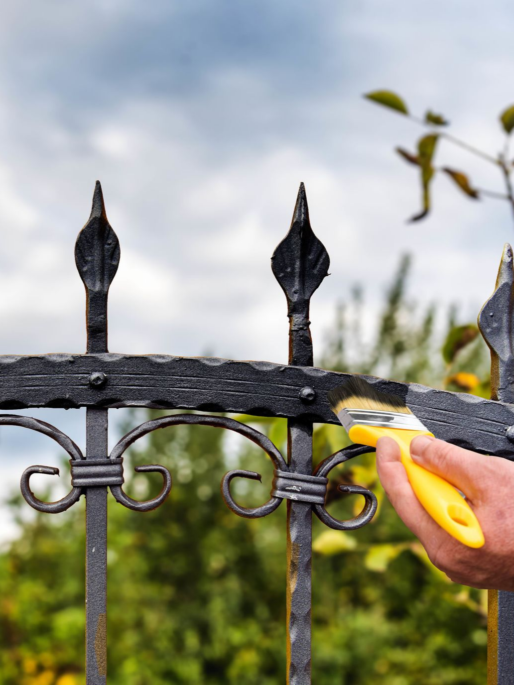 Une main utilisant un outil jaune pour peindre une clôture métallique en noir