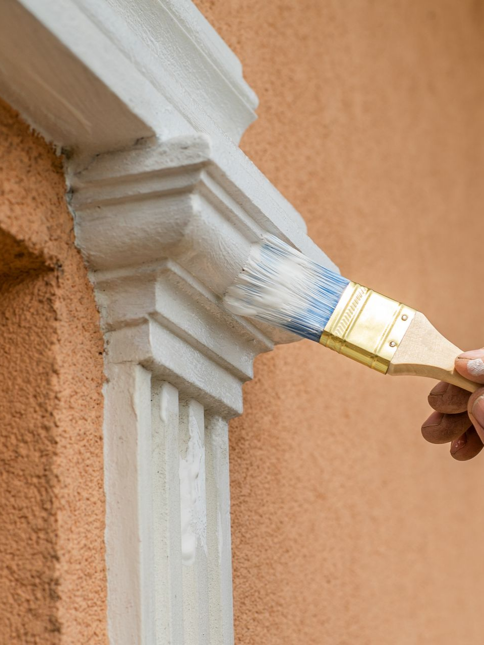 Peinture de boiseries blanches au pinceau sur un mur extérieur couleur pêche