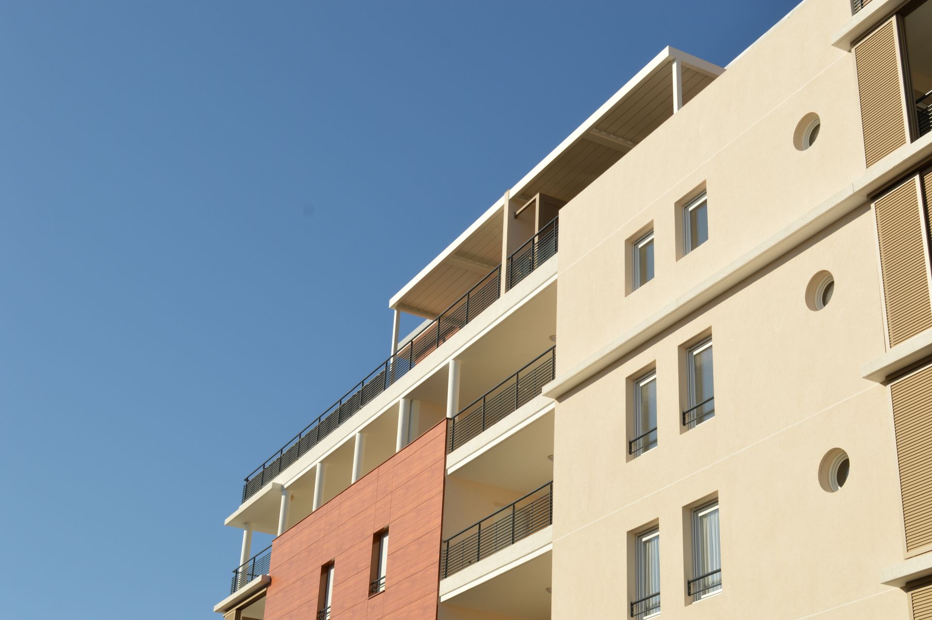 Immeuble résidentiel de plusieurs étages avec un balcon et des portes de garage dans une rue tranquille