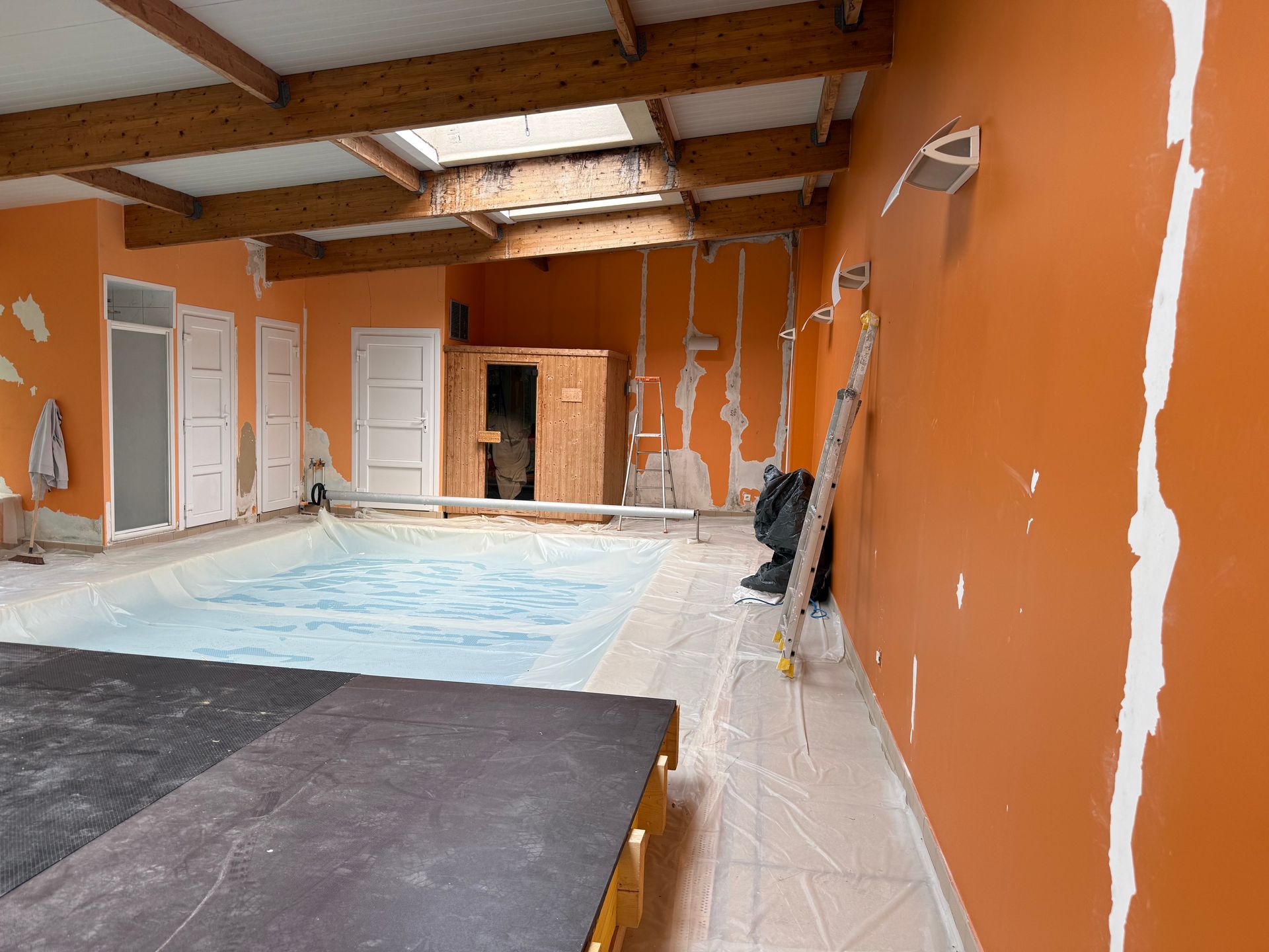 Piscine intérieure dans une pièce aux murs orange en rénovation et poutres apparentes en bois