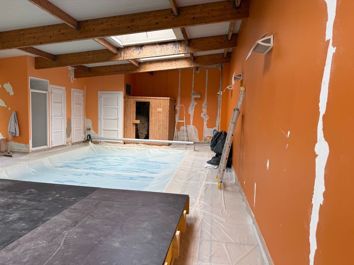 Piscine intérieure dans une pièce aux murs orange en rénovation et poutres apparentes en bois