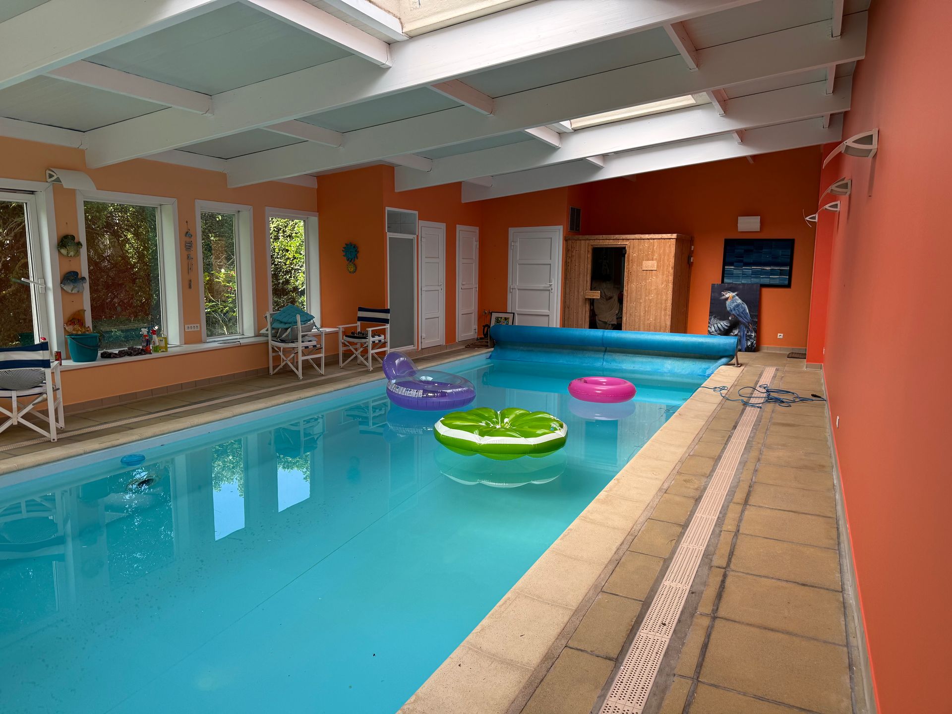 Piscine intérieure dans une pièce aux murs orange rénovés, avec poutres apparentes repeintes