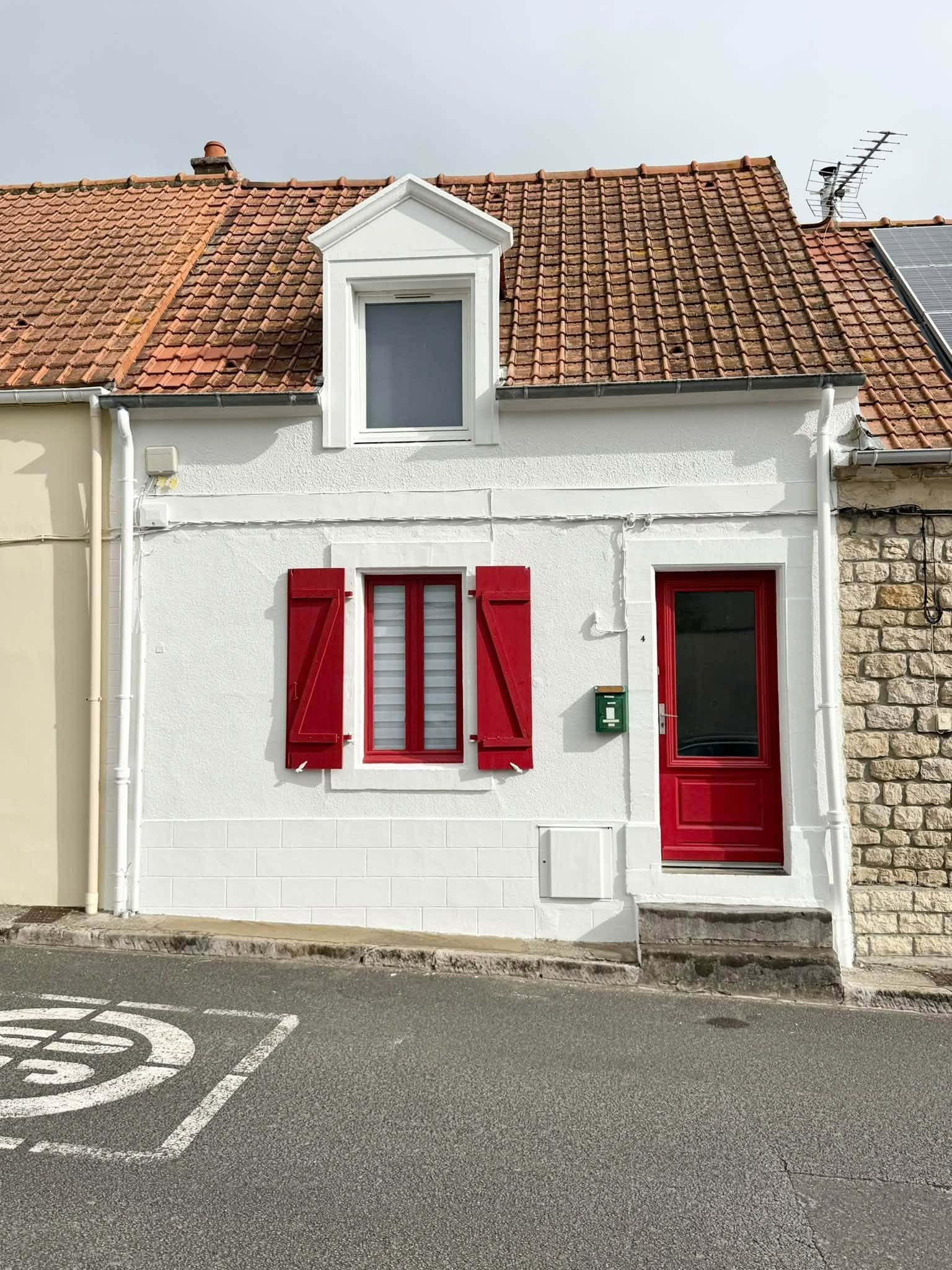 Petite maison blanche aux volets et à la porte rouges, dans une rue calme