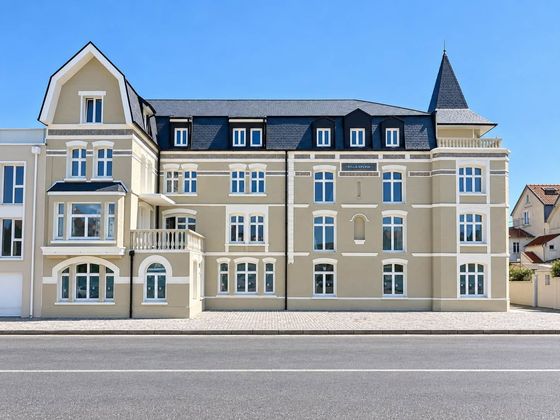 Bâtiment à la façade blanche rénovée et au toit sombre, sous un ciel bleu