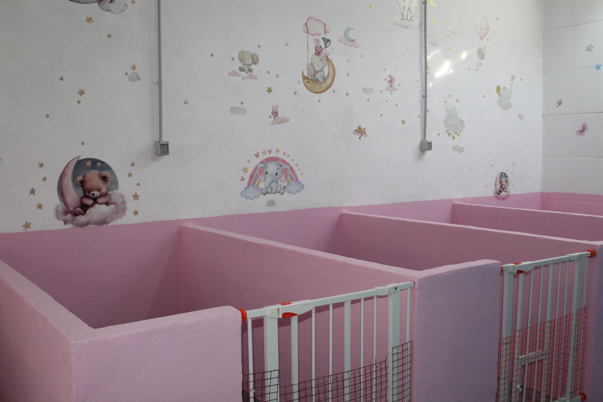 Cubículos rosas con puertas de seguridad, decorados con animales de dibujos animados, en una habitación.