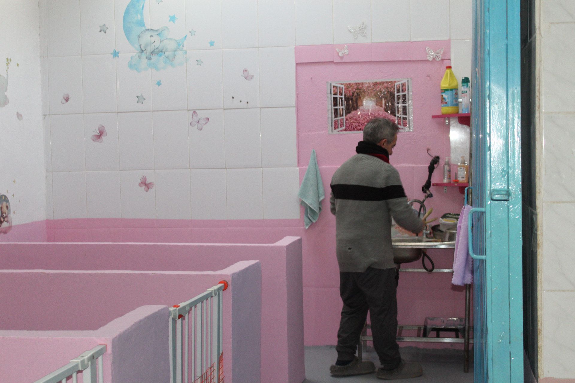 Hombre de gris cerca de una habitación rosa con cunas, posiblemente una guardería.