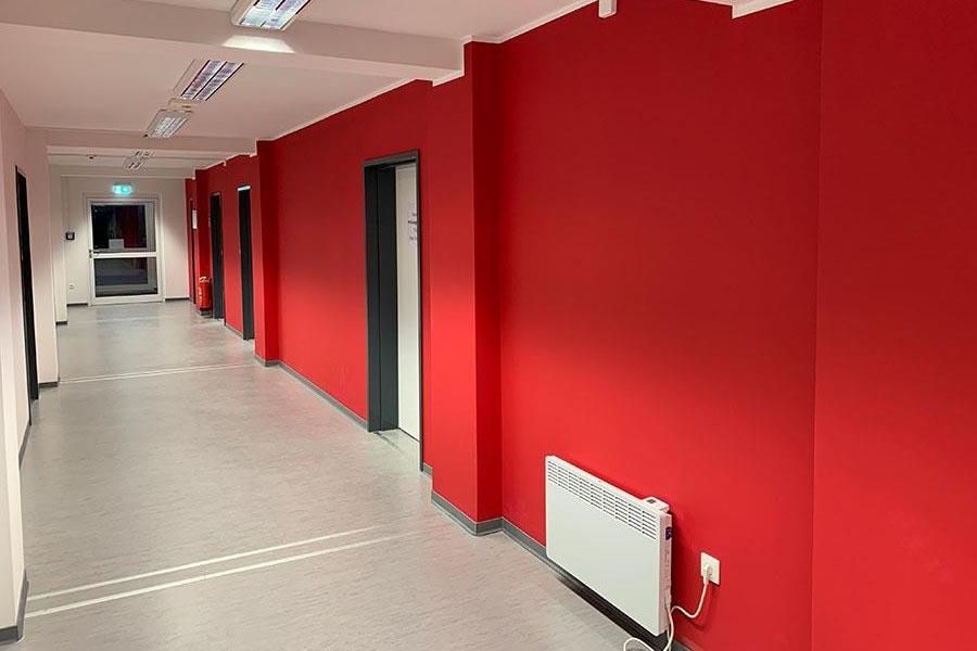 Ein langer Flur mit roten Wänden und einem weißen Heizkörper