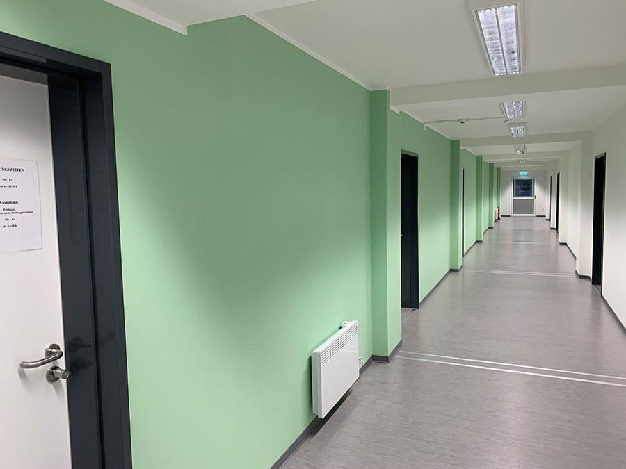 Ein langer Flur mit grünen Wänden und weißen Türen.