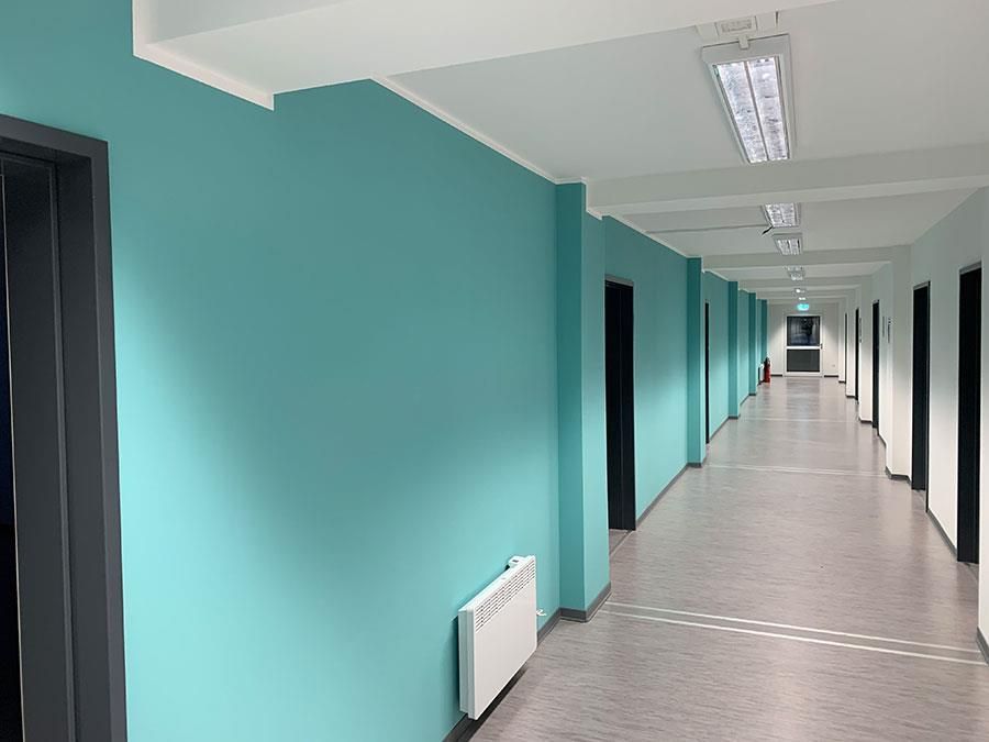Ein langer Flur mit blauen Wänden und schwarzen Türen