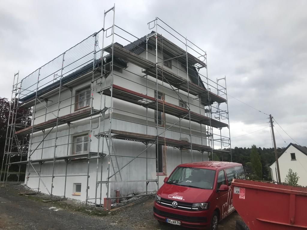 Ein roter Lieferwagen steht vor einem im Bau befindlichen Gebäude.