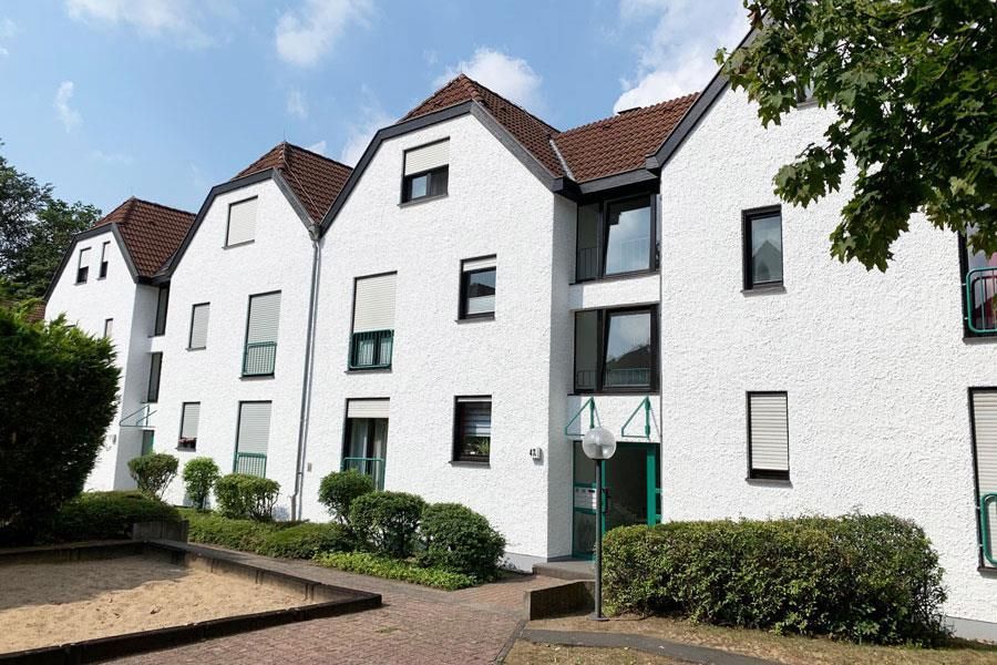 Ein weißes Gebäude mit einem braunen Dach und einem Sandkasten davor.