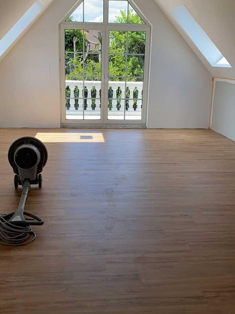 In einem Raum mit einem großen Fenster steht ein Staubsauger auf einem Holzboden.