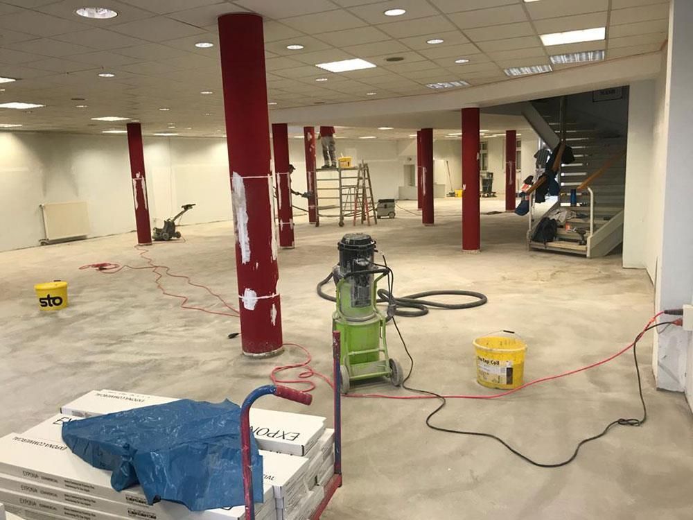 Ein großer leerer Raum mit roten Säulen und einem grünen Staubsauger.