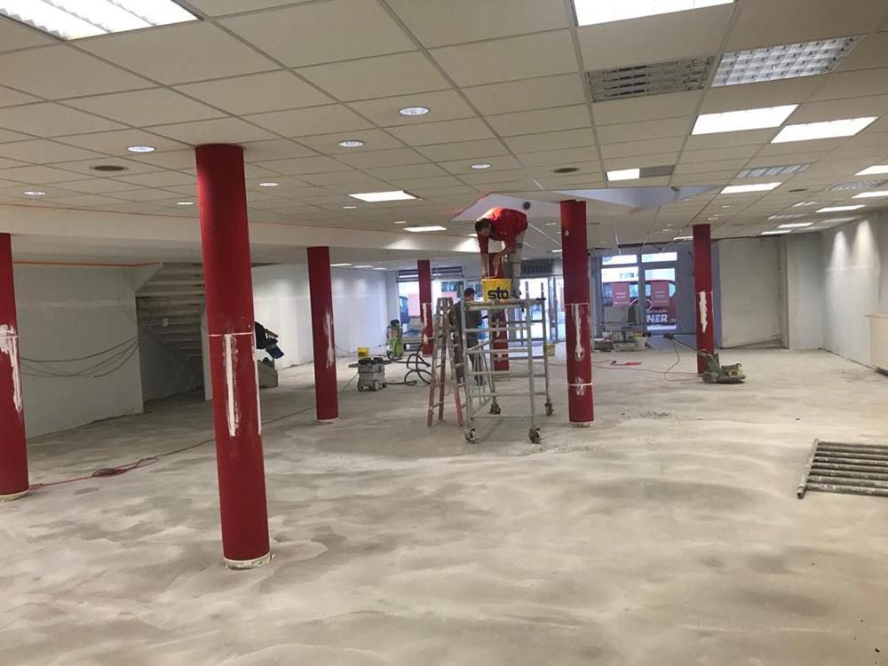 Ein Mann steht auf einer Leiter in einem leeren Raum mit roten Säulen.