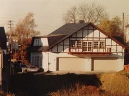 Ein Schwarzweißfoto eines Hauses mit zwei Garagen und einem Balkon.