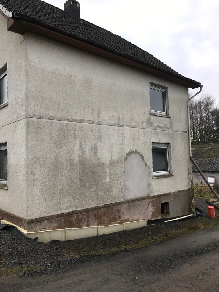 Ein weißes Haus mit schwarzem Dach steht am Straßenrand.