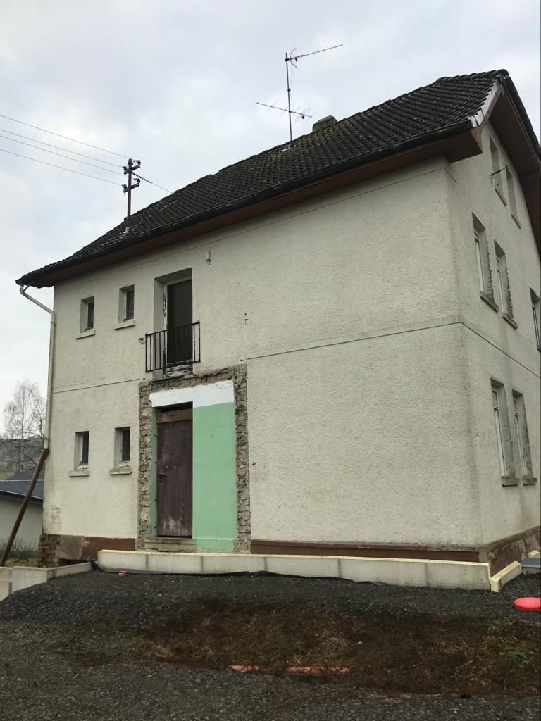 Auf einem Feld steht ein weißes Haus mit schwarzem Dach.