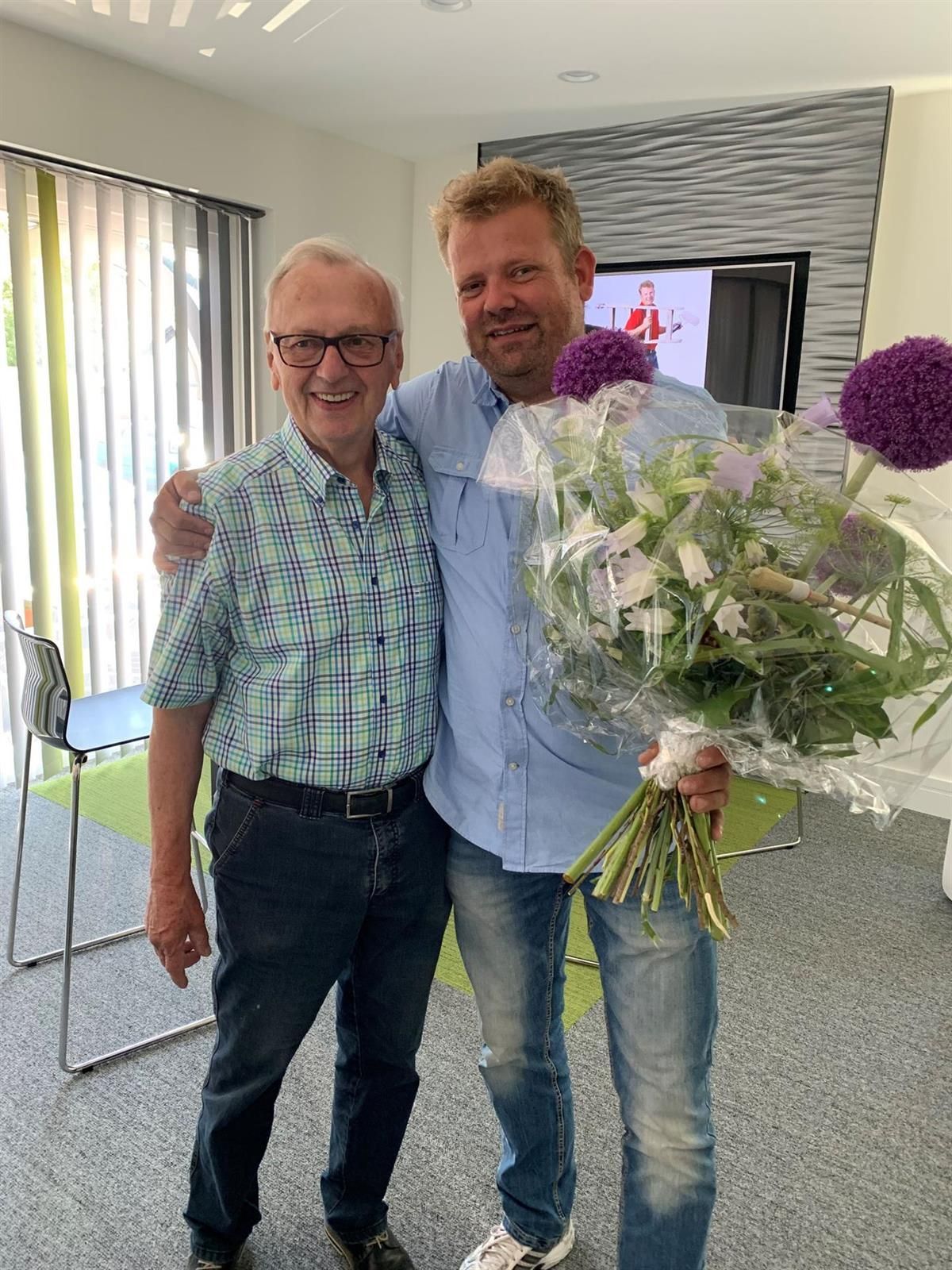 Zwei Männer posieren für ein Foto , einer von ihnen hält einen Blumenstrauß.
