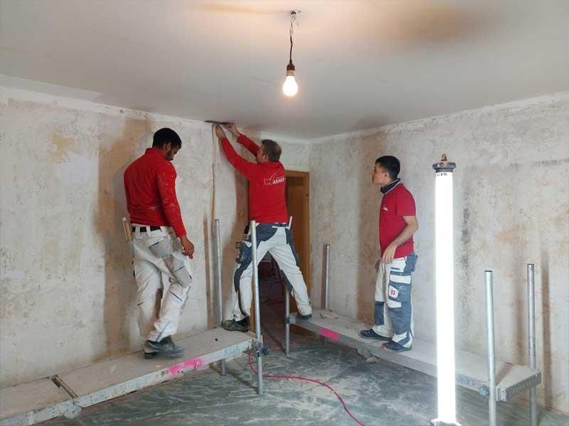 Drei Männer arbeiten an einer Wand in einem Raum.