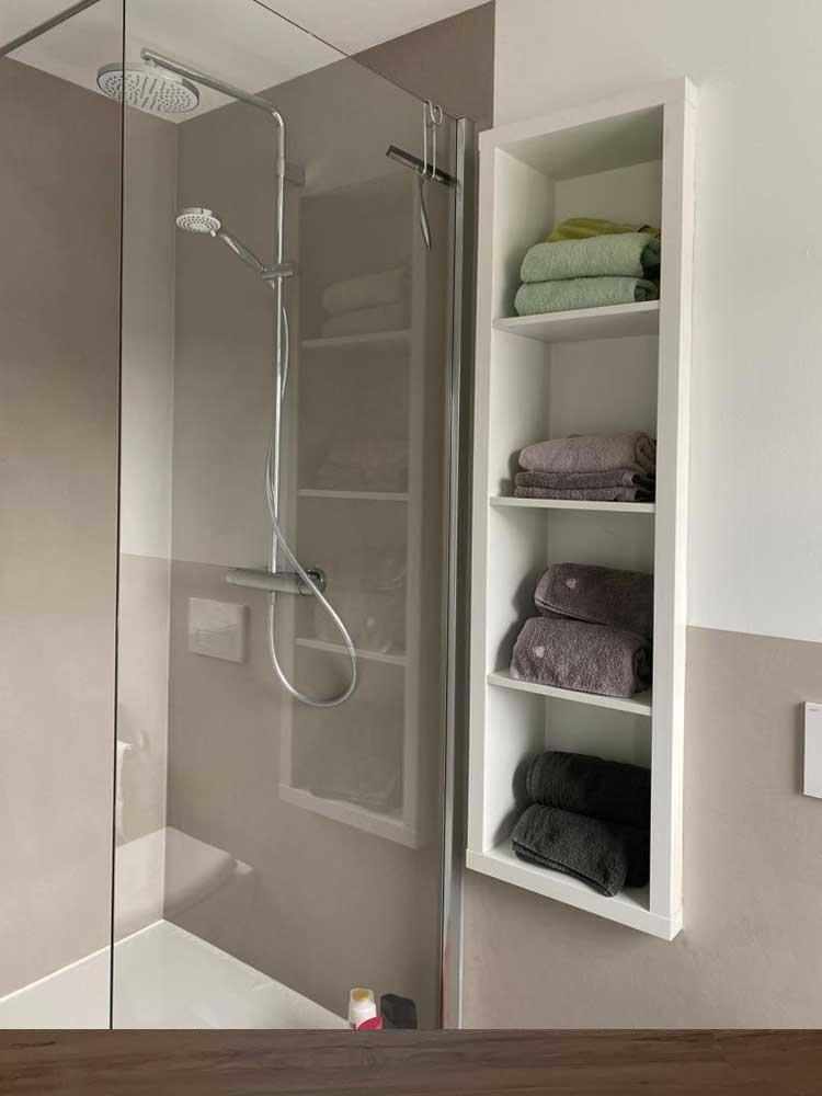 Ein Badezimmer mit Dusche und einem Regal mit Handtüchern darauf.