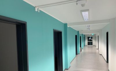 Ein langer Flur mit grünen Wänden und Türen in einem Gebäude.