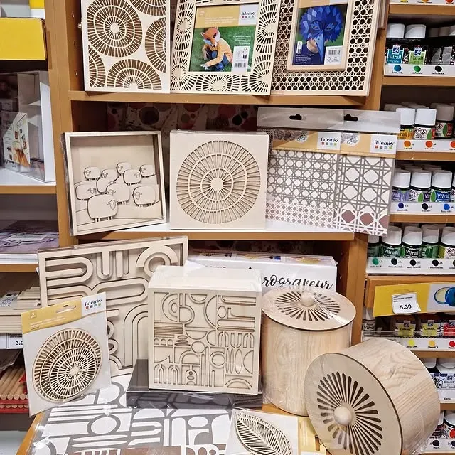 Des étagères dans un magasin d'artisanat présentent des objets d'art en bois, des cadres photo et des boîtes aux motifs géométriques, floraux et animaliers variés.