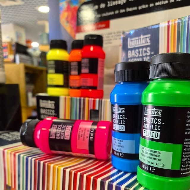 Des flacons de peinture acrylique aux couleurs vives sont disposés sur une surface rayée.