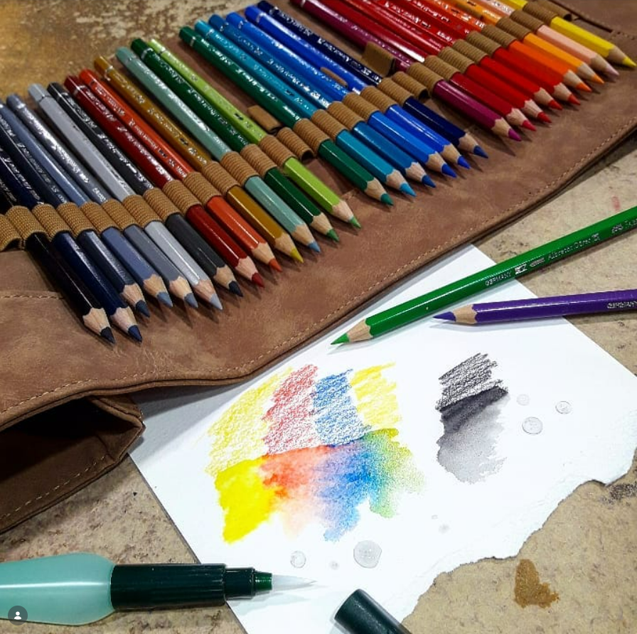 Des crayons de couleur dans un étui enroulable avec un échantillon de couleur sur du papier ; un stylo est posé à proximité.