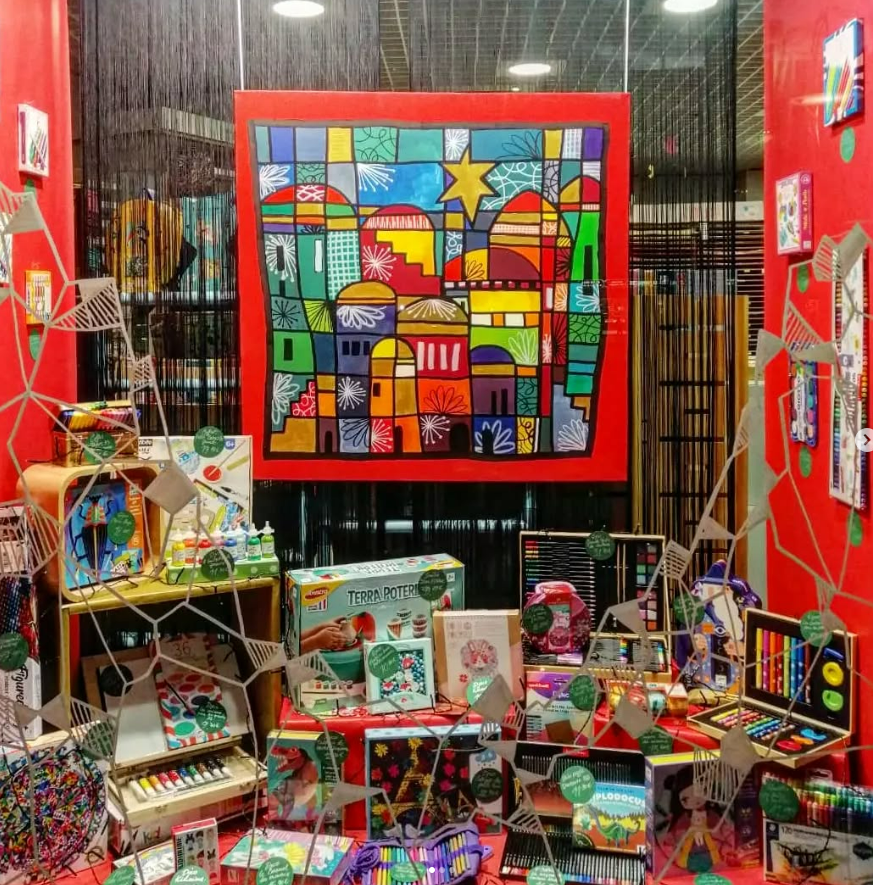 Vitrine de magasin avec une peinture urbaine géométrique et colorée comme point central, entourée de matériel d'art et de livres.