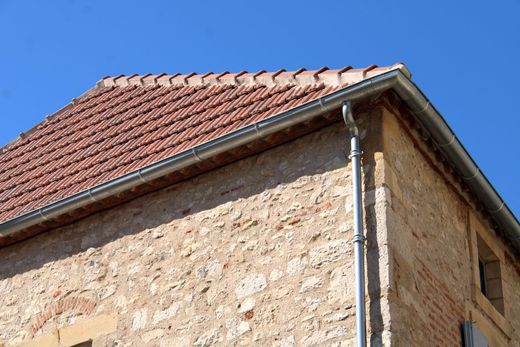 Coin d'un bâtiment en pierre avec toit de tuiles rouges et gouttière.