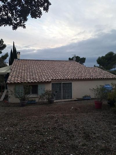 Maison de plain-pied avec toit de tuiles rouges et patio, vue au crépuscule sous un ciel nuageux.