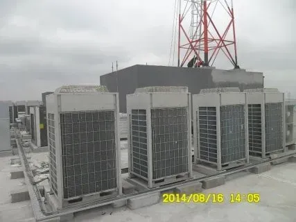 A row of air conditioners on top of a building with a tower in the background.