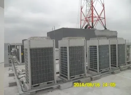 A row of air conditioners on top of a building with a tower in the background.
