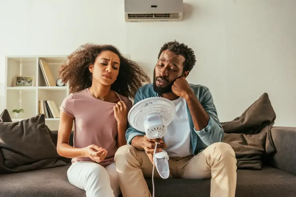 A man and a woman are sitting on a couch holding a fan.