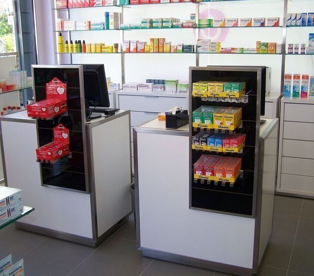 Dos mostradores en una farmacia con estantes llenos de medicamentos.