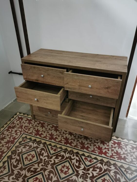Una cómoda de madera con cajones abiertos está colocada sobre un suelo de baldosas.