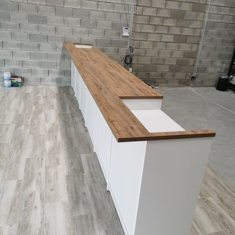 Un mostrador largo con cubierta de madera y gabinetes blancos en una habitación con una pared de ladrillo.