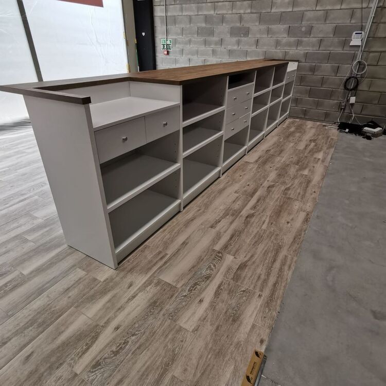 Un mostrador largo con estantes y cajones está colocado sobre un piso de madera en una habitación.