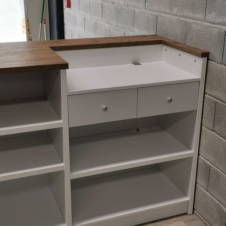 Un mostrador blanco con dos cajones y estantes junto a una pared de ladrillos.