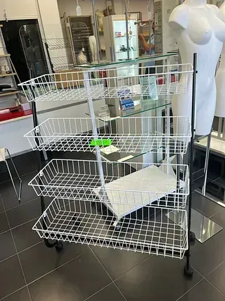 Un carro de alambre con ruedas está sentado sobre un piso de baldosas al lado de un maniquí.